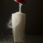 Sugar is poured from a can of coke into a glass.