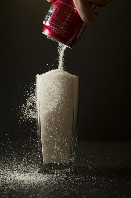Sugar is poured from a can of coke into a glass.